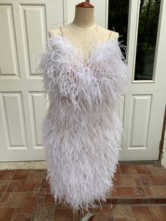 a mannequin wearing a white feathered dress on display in front of a door