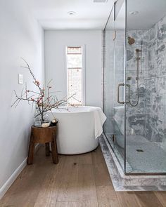 a white bath tub sitting next to a wooden table in a bathroom under a window