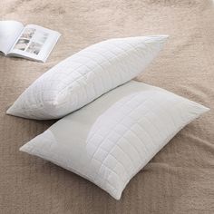 two white pillows sitting on top of a bed next to an open book and magazine