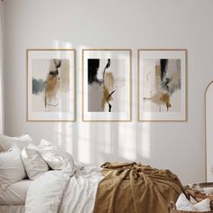 three paintings hang on the wall above a bed in a room with white sheets and pillows