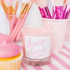 pink cupcakes and makeup brushes are sitting on a table next to a candle