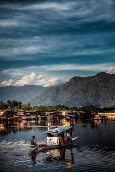 a small boat floating on top of a lake under a cloudy sky with mountains in the background