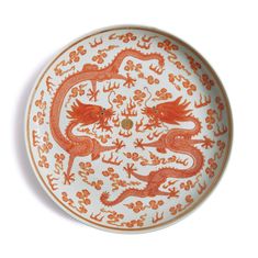 an orange and white plate with two dragon designs on the front, sitting on a white surface