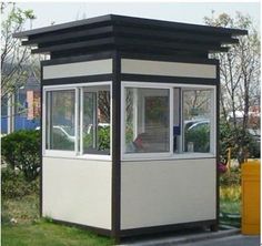 a small white and black building sitting on top of a grass covered field next to a yellow trash can