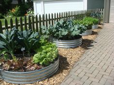 a row of metal planters filled with different types of vegetables in front of a house