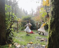 two women in white dresses are playing with a frisbee near some trees and bushes