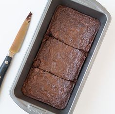 a loaf of brownies in a pan next to a knife on a white table