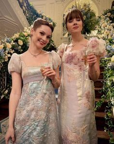 two women in dresses standing next to each other holding wine glasses and posing for the camera