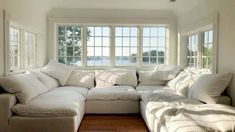 a large white couch sitting in a living room next to a window with lots of pillows on it