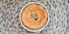 a white bowl filled with hummus sitting on top of a woven place mat