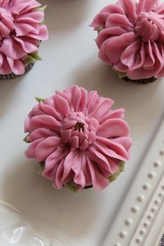 four cupcakes with pink frosting and green leaves on top are sitting on a white tray