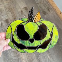 a hand holding up a stained glass pumpkin with a face on it's side