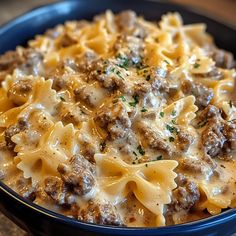 a blue bowl filled with pasta covered in cheese and meat sauce on top of a wooden table