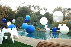 some white and blue balloons are floating in the air near a swimming pool with chairs