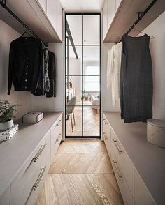 a walk - in closet with white cabinets and wooden flooring, open glass doors leading to the bedroom