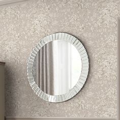 a round mirror hanging on the wall above a dresser in a room with floral wallpaper