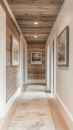 a long hallway with wood paneling and pictures on the wall along one side that leads to another room