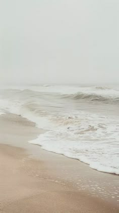 an empty beach with waves coming in to shore and one person walking on the sand