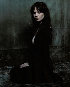 a woman sitting on the ground in a dark room with her hands behind her back