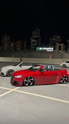 two cars parked in a parking lot with city lights in the background