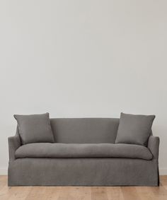 a gray couch sitting on top of a wooden floor next to a white wall with two pillows