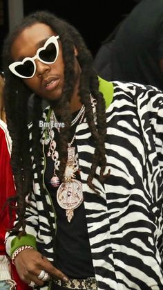 a man with long dreadlocks and sunglasses on sitting next to a woman in a zebra print jacket