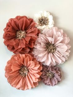 four different colored paper flowers on a white surface