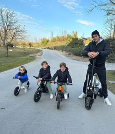 three young boys are riding their bikes down the street with an adult standing next to them