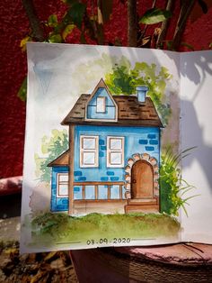 a drawing of a blue house on a piece of paper next to a potted plant