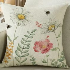 a pillow with flowers and bees on it sitting on a couch next to a window