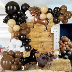 an assortment of balloons and horses on display in front of a wooden wall with hay bales