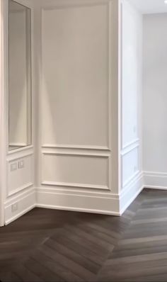 an empty room with white walls and wood flooring is pictured in this image, there are two mirrors on the wall