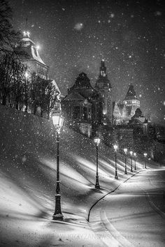 a black and white photo of a snowy night in the city with street lights on