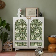 a white cabinet sitting on top of a hard wood floor next to a green wall