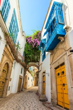 an alleyway with blue and yellow doors and flowers growing on the balconies