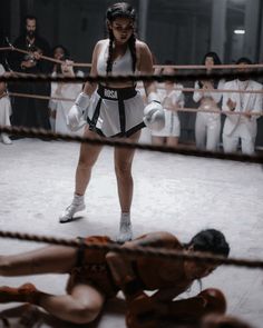 two women in white boxing outfits stand next to each other as others watch from the ropes