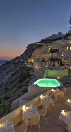 an outdoor dining area with white tables and chairs overlooking the ocean at night, lit up by candles