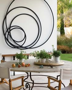 an outdoor table with chairs and potted plants on it in front of a wall sculpture