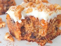 a piece of carrot cake with white frosting and walnuts on the top, sitting on a plate