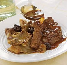 a white plate topped with meat and vegetables covered in gravy next to a glass of water