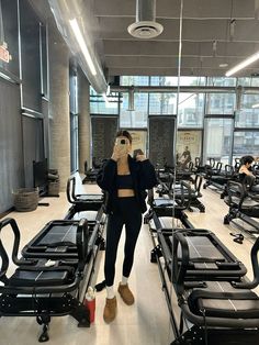 a woman taking a selfie in front of an exercise room with rows of treadmills