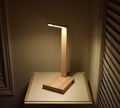 a wooden lamp sitting on top of a table next to a window with shutters