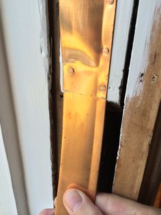 a hand is holding the door handle on an open door with white paint and brown trim