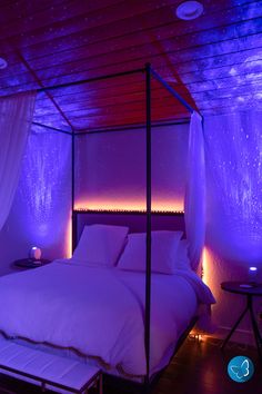 a bed with white sheets and purple lights in a room that is lit up at night