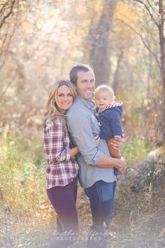 a man and woman holding a baby in the woods