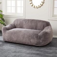 a gray couch sitting on top of a carpeted floor next to a mirror and potted plant