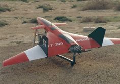 a small red and white airplane sitting on top of a dirt field in the desert