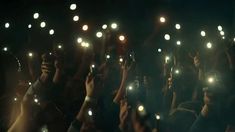 many people holding up their cell phones in the air at night with lights shining on them