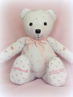 a white teddy bear with pink hearts on it's chest sitting against a pink background