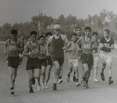 an old black and white photo of men running in a race with trees in the background